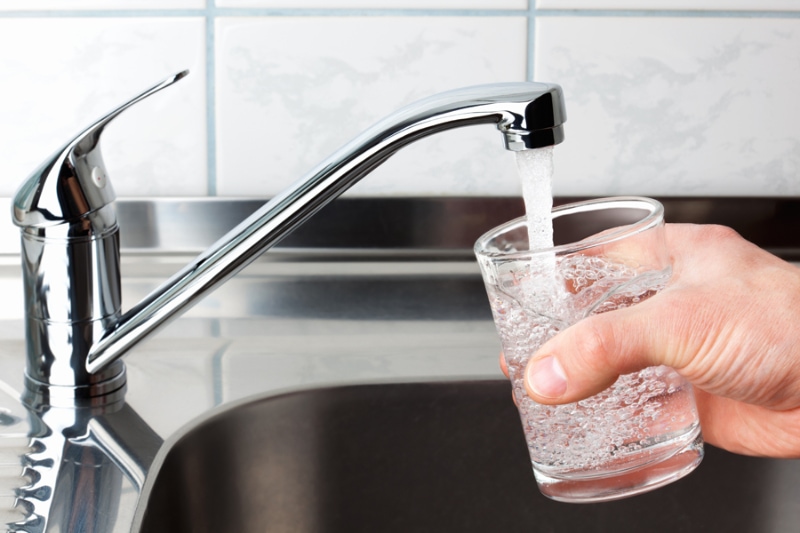 What Causes Sewage Backup? Hand holding a glass of water poured from the kitchen faucet.